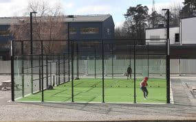 Partido de padel en una pista exterior con paredes de cristal y cesped verde, dos jugadores en plena accion de juego