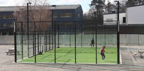 Partido de padel en una pista exterior con paredes de cristal y cesped verde, dos jugadores en plena accion de juego