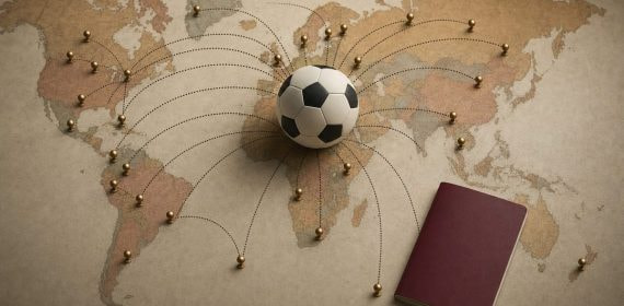 Balón de fútbol en el centro de un mapamundi con chinchetas doradas unidas por líneas hacia varios países