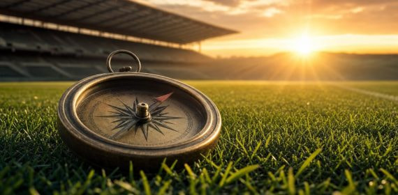 Brújula de latón sobre el césped de un estadio vacío apunta al horizonte al amanecer rumbo al Mundial 2030