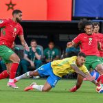 Bruno Guimarães cae al césped disputando el balón ante dos rivales de Marruecos en el Mundial 2026.