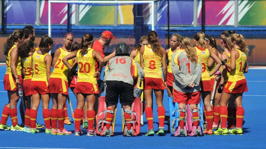 Las jugadoras de la selección española femenina de hockey hierba forman corro con el técnico sobre el campo azul