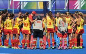 Las jugadoras de la selección española femenina de hockey hierba forman corro con el técnico sobre el campo azul