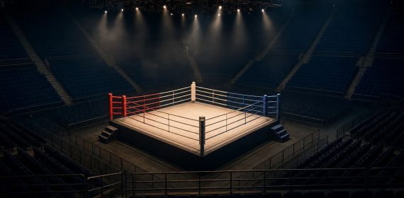 Ring de boxeo vacío iluminado por focos en el centro de un pabellón a oscuras con las gradas sin público