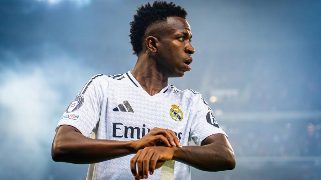 Vinícius Júnior, con la camiseta blanca del Real Madrid, mira hacia un lado durante un partido nocturno.