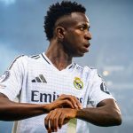 Vinícius Júnior, con la camiseta blanca del Real Madrid, mira hacia un lado durante un partido nocturno.