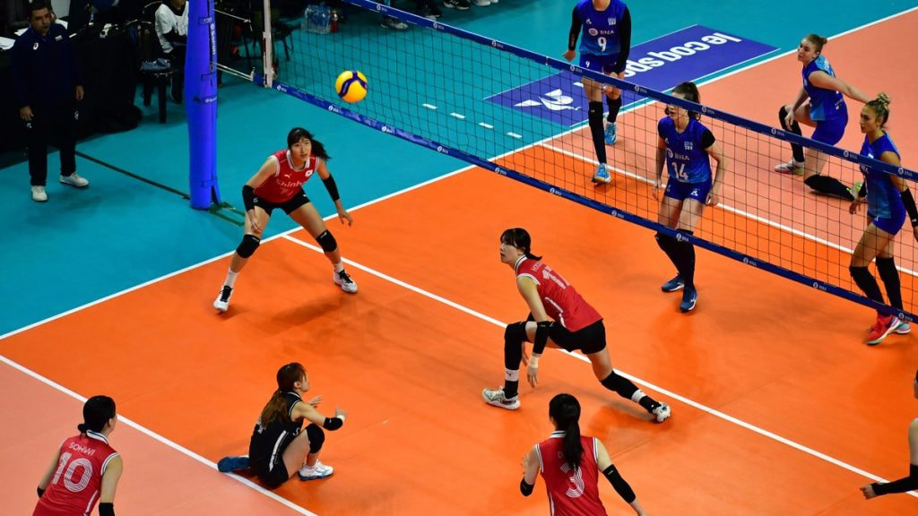 Una jugadora se prepara para recibir el balón junto a la red en un partido de voleibol femenino