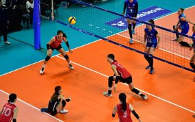 Una jugadora se prepara para recibir el balón junto a la red en un partido de voleibol femenino