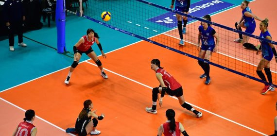 Una jugadora se prepara para recibir el balón junto a la red en un partido de voleibol femenino