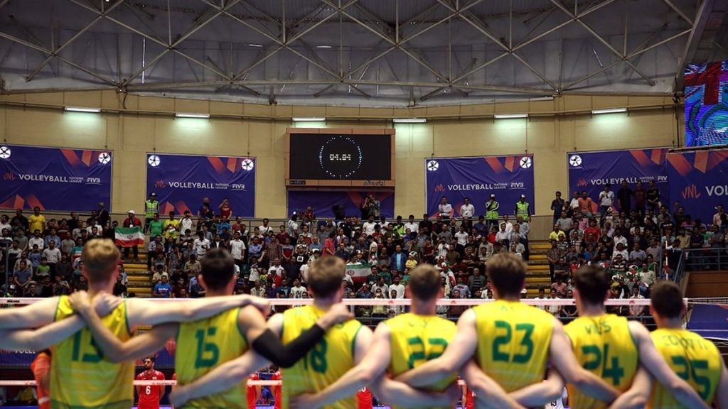 Dos equipos alineados ante la red en un pabellón lleno y forrado de vallas de la Volleyball Nations League