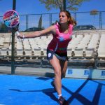 Una jugadora de pádel golpea la bola con la pala en una pista azul al aire libre