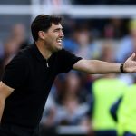 El entrenador Andoni Iraola, vestido de negro, extiende el brazo derecho para dar una orden a sus jugadores junto a la línea de banda