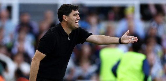 El entrenador Andoni Iraola, vestido de negro, extiende el brazo derecho para dar una orden a sus jugadores junto a la línea de banda
