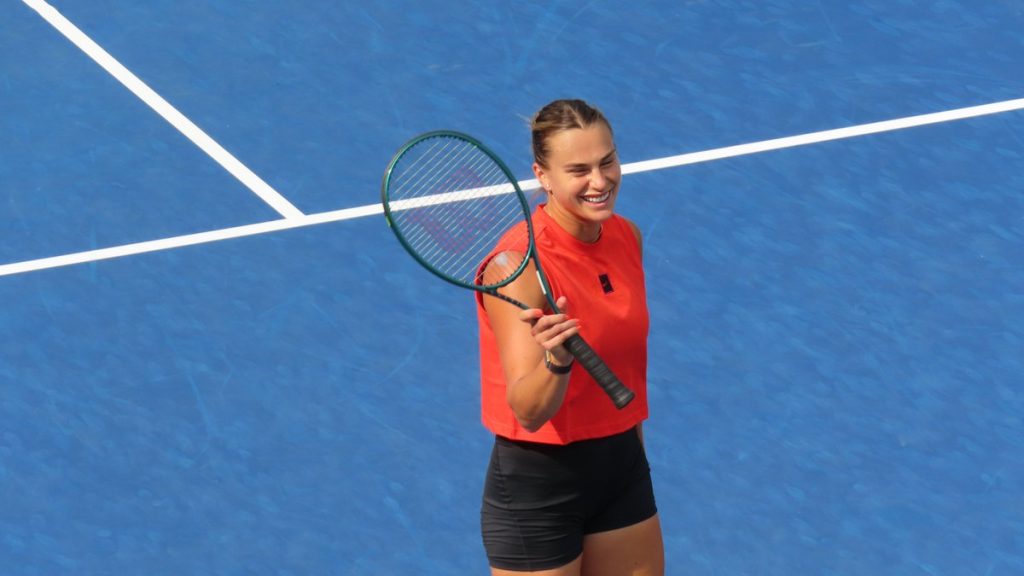 Aryna Sabalenka sonríe con la raqueta en la mano sobre una pista dura azul durante un entrenamiento