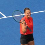 Aryna Sabalenka sonríe con la raqueta en la mano sobre una pista dura azul durante un entrenamiento