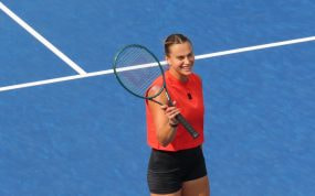 Aryna Sabalenka sonríe con la raqueta en la mano sobre una pista dura azul durante un entrenamiento