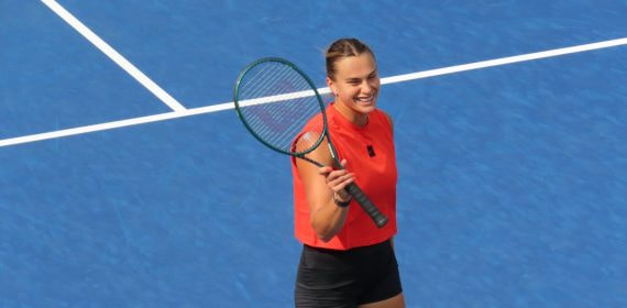 Aryna Sabalenka sonríe con la raqueta en la mano sobre una pista dura azul durante un entrenamiento