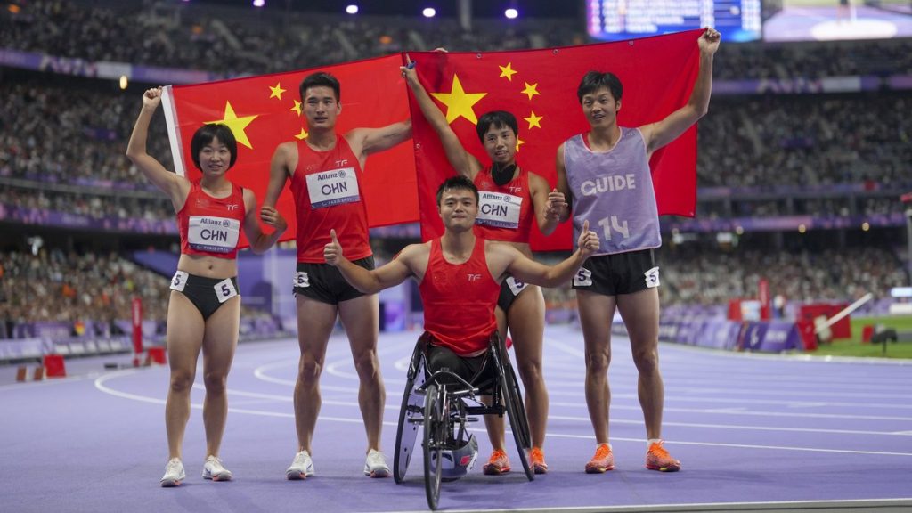 Cinco integrantes del equipo paralímpico chino celebran con la bandera de su país sobre la pista de atletismo