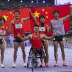 Cinco integrantes del equipo paralímpico chino celebran con la bandera de su país sobre la pista de atletismo