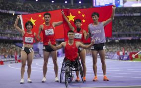 Cinco integrantes del equipo paralímpico chino celebran con la bandera de su país sobre la pista de atletismo