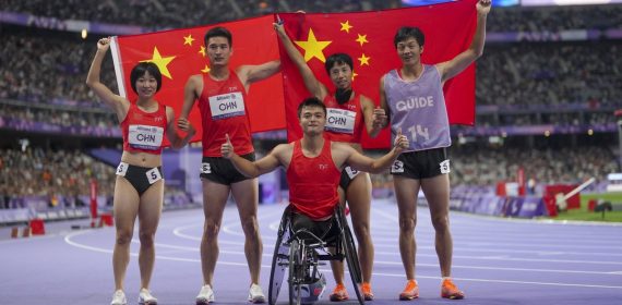 Cinco integrantes del equipo paralímpico chino celebran con la bandera de su país sobre la pista de atletismo