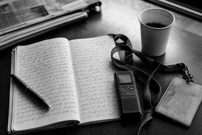Libreta de reportero con notas manuscritas, grabadora y acreditación de prensa sobre una mesa de redacción