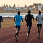 Jóvenes atletas corriendo de espaldas por una pista de atletismo junto al océano en una ciudad de África Occidental