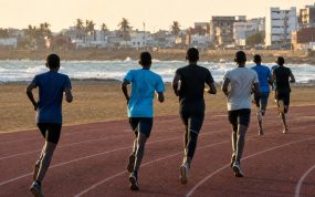 Jóvenes atletas corriendo de espaldas por una pista de atletismo junto al océano en una ciudad de África Occidental