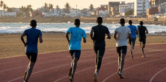 Jóvenes atletas corriendo de espaldas por una pista de atletismo junto al océano en una ciudad de África Occidental