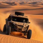 Prototipo de rally-raid sin distintivos coronando una duna y levantando una nube de arena en el desierto