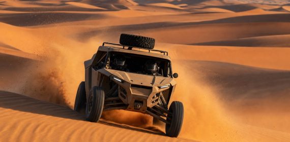 Prototipo de rally-raid sin distintivos coronando una duna y levantando una nube de arena en el desierto