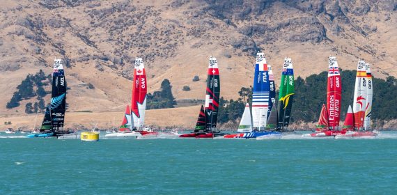 La flota de catamaranes F50 de SailGP navega en línea durante una regata, con el barco español a la derecha