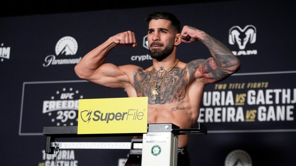 Ilia Topuria flexiona los brazos sobre la báscula durante el pesaje oficial del UFC Freedom 250