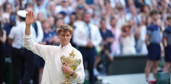 Jannik Sinner saluda al público con el trofeo de ganador de Wimbledon 2026 en sus brazos.