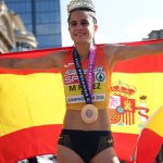 María Pérez despliega la bandera de España con la medalla al cuello y una corona en la cabeza tras ganar el medio maratón marcha
