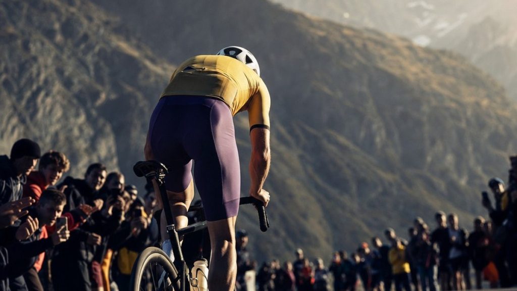 Ciclista de espaldas atacando en la subida a un puerto de montaña entre el público