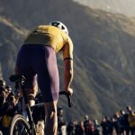 Ciclista de espaldas atacando en la subida a un puerto de montaña entre el público