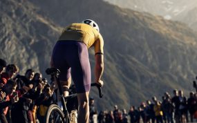 Ciclista de espaldas atacando en la subida a un puerto de montaña entre el público