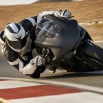 Una moto de competición inclinada al límite con la rodilla del piloto rozando el asfalto en la salida de una curva
