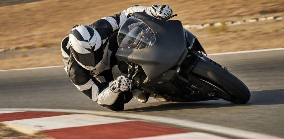 Una moto de competición inclinada al límite con la rodilla del piloto rozando el asfalto en la salida de una curva