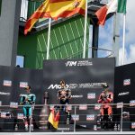 Los tres pilotos del podio de Moto3 sobre el cajón del Gran Premio de Alemania, con la bandera española ondeando detrás