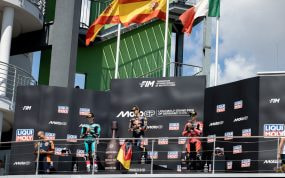 Los tres pilotos del podio de Moto3 sobre el cajón del Gran Premio de Alemania, con la bandera española ondeando detrás