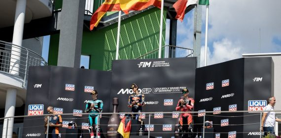 Los tres pilotos del podio de Moto3 sobre el cajón del Gran Premio de Alemania, con la bandera española ondeando detrás