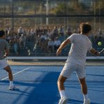 Dos jugadores de pádel disputan un punto en una pista exterior acristalada con público en la grada
