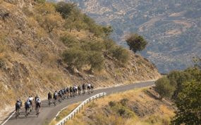 El pelotón asciende en fila por una carretera de montaña entre laderas secas y olivos del sur de España