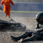 Un piloto sentado en la grava se sujeta el hombro tras una caída mientras los comisarios acuden hacia él