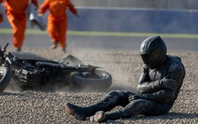 Un piloto sentado en la grava se sujeta el hombro tras una caída mientras los comisarios acuden hacia él