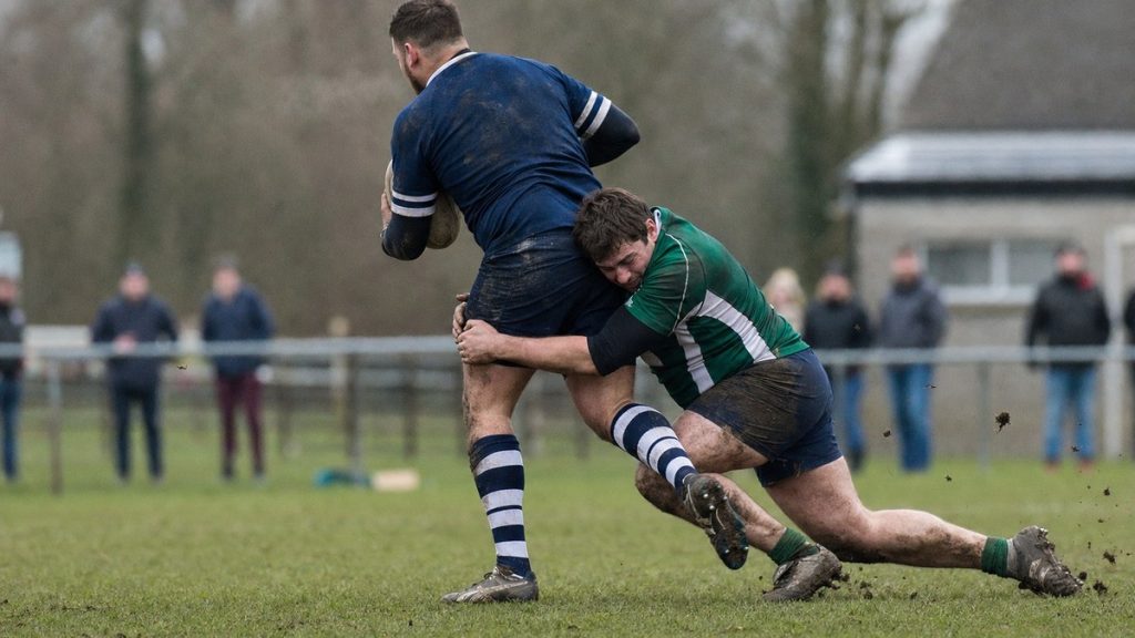 Un jugador de rugby amateur placa a la altura de la cintura con la cabeza a un lado en un campo municipal