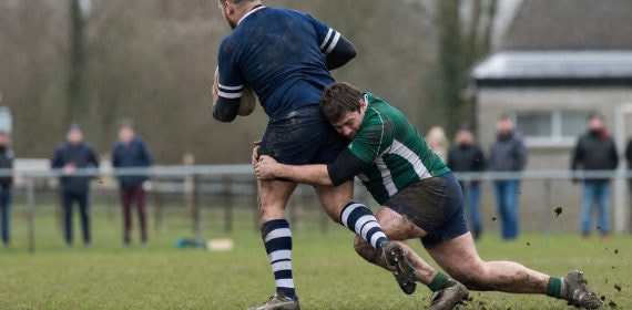 Un jugador de rugby amateur placa a la altura de la cintura con la cabeza a un lado en un campo municipal