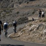 Tres ciclistas ascienden una curva de herradura en un puerto de montaña seco con público en la cuneta